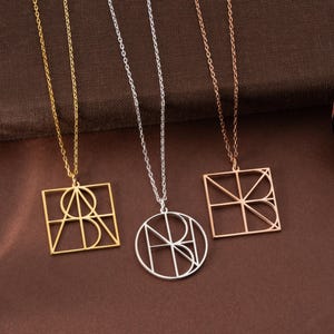 May include: Three pendant necklaces with geometric designs. One is gold, square-shaped with a circle and lines. The second is silver, circular with lines. The third is rose gold, square-shaped with lines. All have delicate chains.