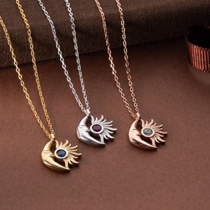 Pode incluir: Três colares com pingentes celestiais. Os pingentes apresentam um design de lua crescente e sol, cada um com um centro de pedra preciosa. As correntes e os pingentes são nas cores ouro, prata e ouro rosa. As pedras preciosas são azuis, vermelhas e verdes.