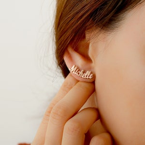 May include: Gold-toned nameplate earrings with the name "Michelle" spelled out in a cursive font.