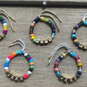 May include: Five colorful beaded bracelets with gold letter beads spelling out the name "JRAD".