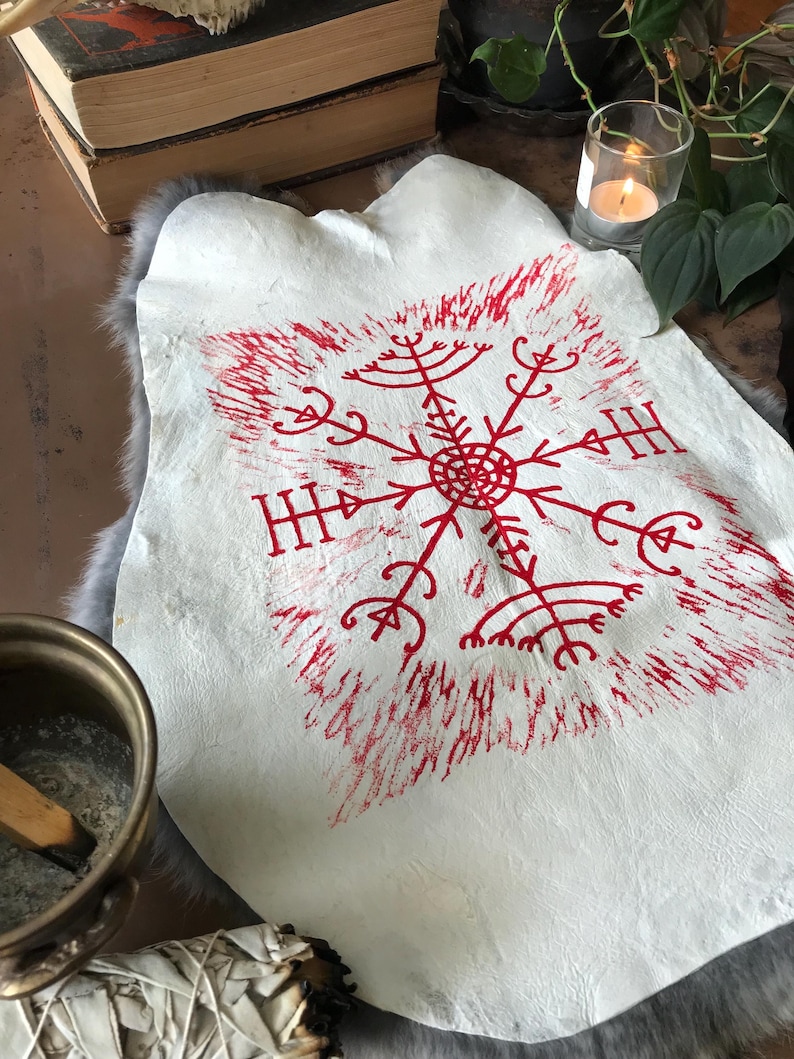 May include: A white leather hide with a red, stylized snowflake design. The design is centered on the hide and has a textured, hand-printed appearance. The hide is displayed on a gray fur-like surface.