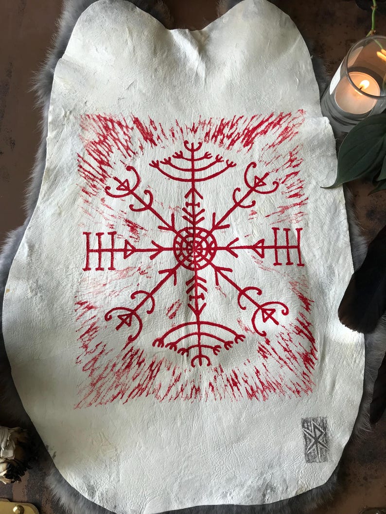 May include: A white leather hide with a red, stylized, symmetrical design in the center. The design is a series of lines and shapes radiating from a central circle. The hide is on a gray, furry surface.