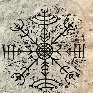 May include: A black, stylized Viking compass symbol, known as Vegv&iacute;sir, is printed on a textured, off-white surface. The symbol is a complex, symmetrical design with multiple arms radiating from a central circle.