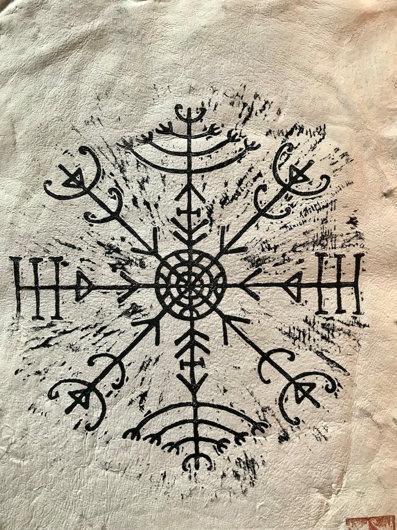 May include: A black, stylized Viking compass symbol, known as Vegv&iacute;sir, is printed on a textured, off-white surface. The symbol is a complex, symmetrical design with multiple arms radiating from a central circle.