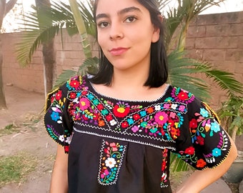 May include: Black embroidered blouse with colorful floral designs. The blouse has a round neckline and short sleeves. The text "SIZES S" is visible on the front of the blouse.