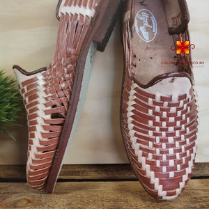 K&ouml;nnte beinhalten: Ein Paar braune Ledersandalen mit gewebtem Design. Die Sandalen haben ein wei&szlig;es Lederfutter und eine braune Ledersohle.
