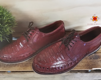 May include: A pair of burgundy leather shoes with a woven design on the sole. The shoes have a lace-up closure and a glossy finish. The text "COLORES DE MEXICO MX" is visible on the right shoe.