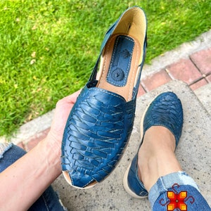 May include: A pair of blue leather sandals with a woven design. The sandals have a pointed toe and a flat sole.