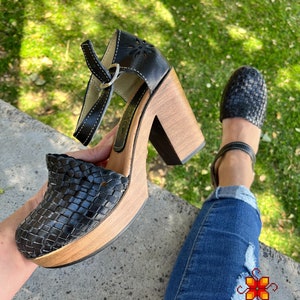 Op de afbeelding: Zwarte geweven platform sandalen van leer met een houten hak. De sandalen hebben een band met een gespsluiting.