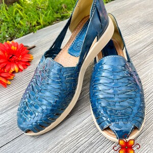 May include: A pair of blue leather sandals with a woven design. The sandals have a white sole and are open-toed.
