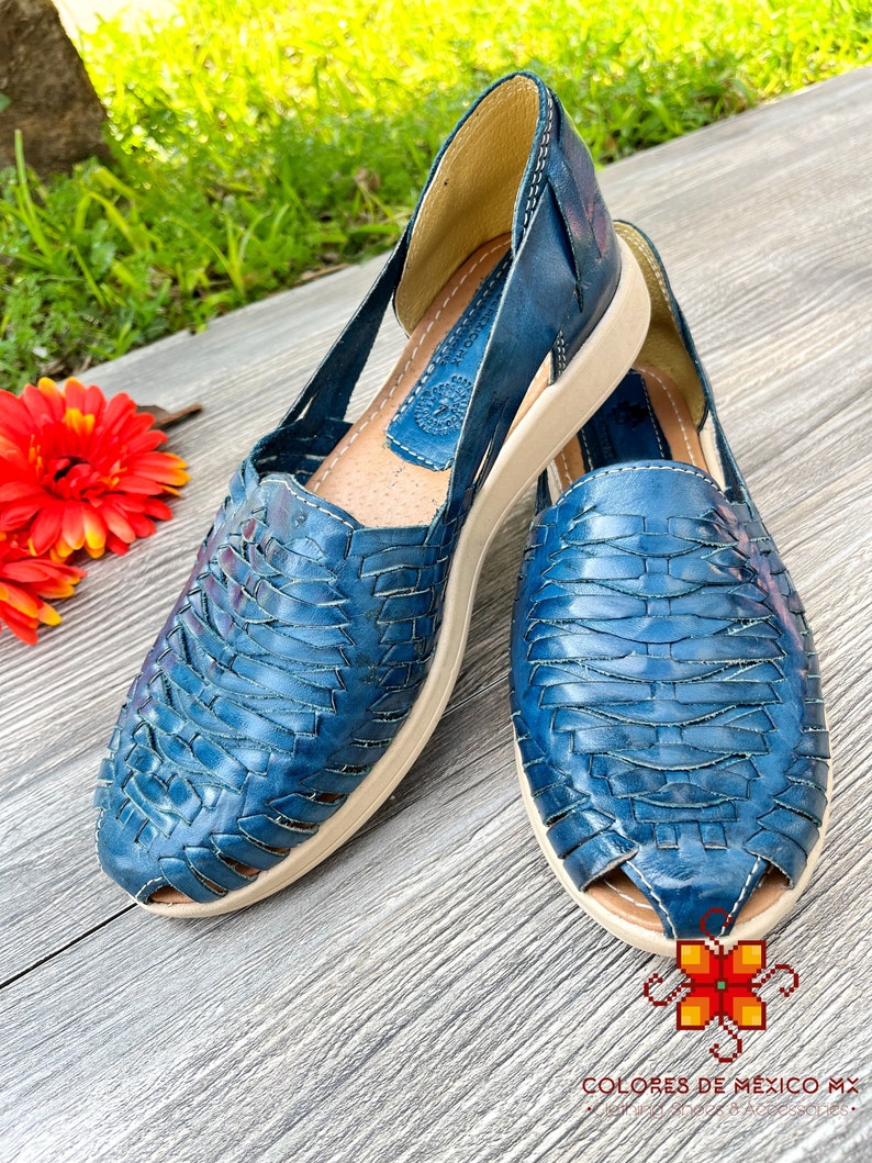 May include: A pair of blue leather sandals with a woven design. The sandals have a white sole and are open-toed.