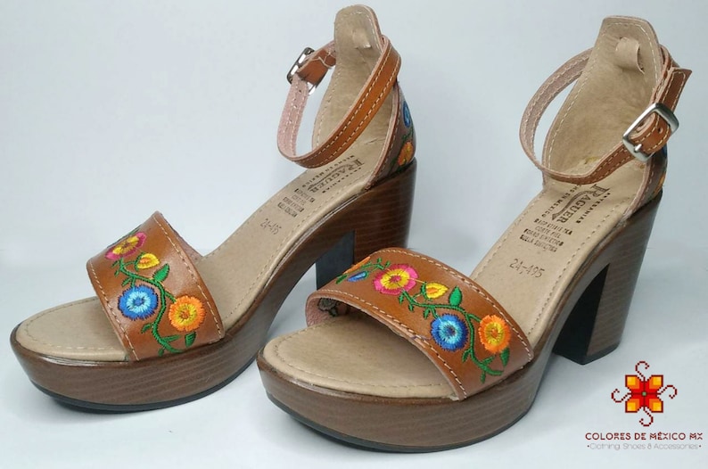 May include: A pair of brown leather sandals with colorful embroidered flowers. The sandals have a chunky heel and an ankle strap.