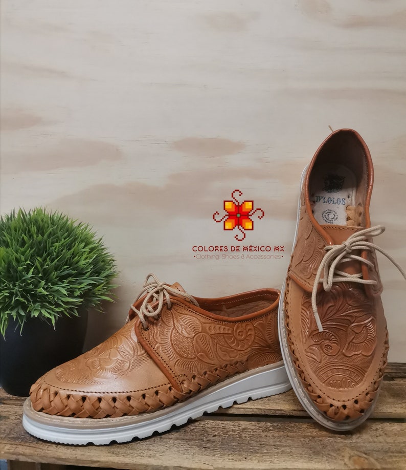 K&ouml;nnte beinhalten: Ein Paar braune Lederschuhe mit aufwendigen Blumenmustern. Die Schuhe haben wei&szlig;e Sohlen und Schn&uuml;rsenkel. Die Schuhe sind in Mexiko hergestellt.