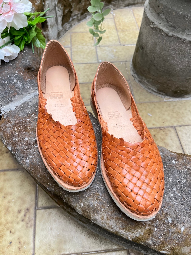 Pu&ograve; includere: Un paio di sandali piatti in pelle intrecciata marroni. I sandali hanno un design semplice e sono realizzati in pelle morbida e flessibile.