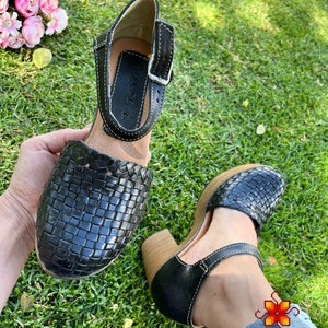 Op de afbeelding: Zwarte leren geweven platform sandalen met een gespsluiting en een houten hak. De sandalen hebben een wit stiksel detail.