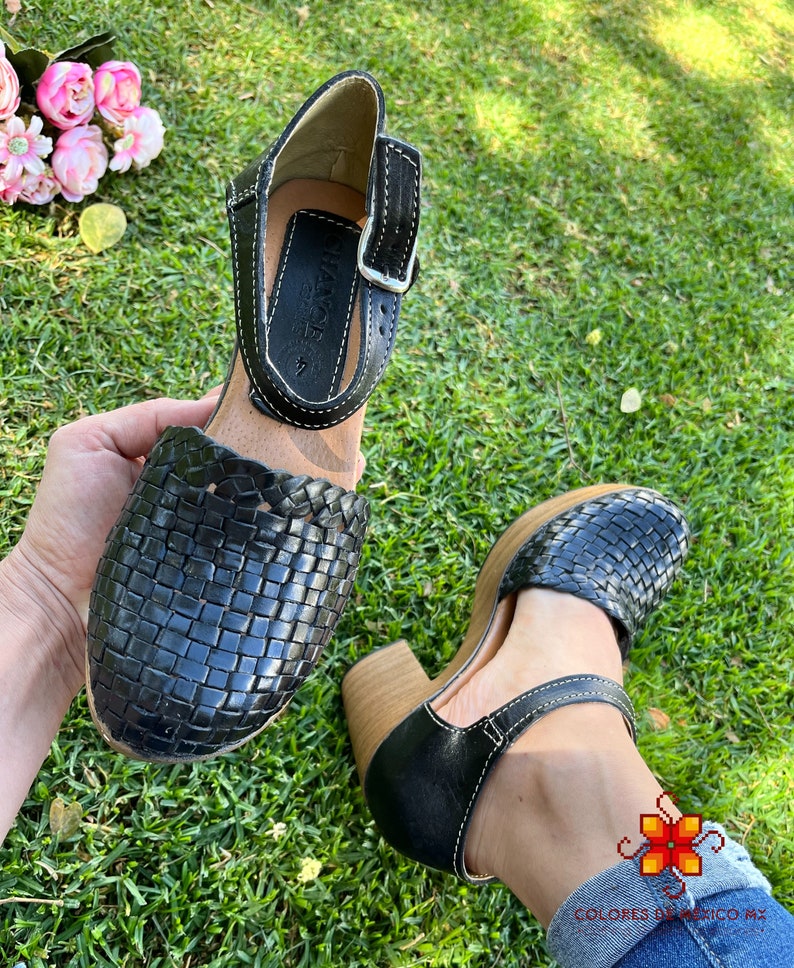 Op de afbeelding: Zwarte leren geweven platform sandalen met een gespsluiting en een houten hak. De sandalen hebben een wit stiksel detail.