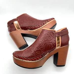 May include: A pair of brown leather heeled shoes with a floral embossed design. The shoes have a wooden platform and a chunky heel.