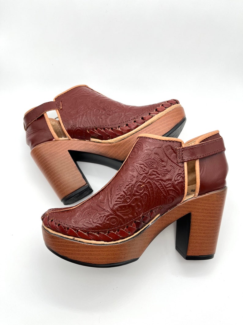 May include: A pair of brown leather heeled shoes with a floral embossed design. The shoes have a wooden platform and a chunky heel.