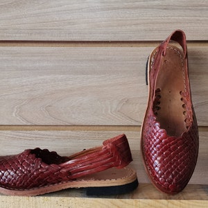Puede incluir: Un par de sandalias de cuero marr&oacute;n con un dise&ntilde;o tejido. Las sandalias tienen una correa que va alrededor del tobillo y un dedo del pie cerrado.