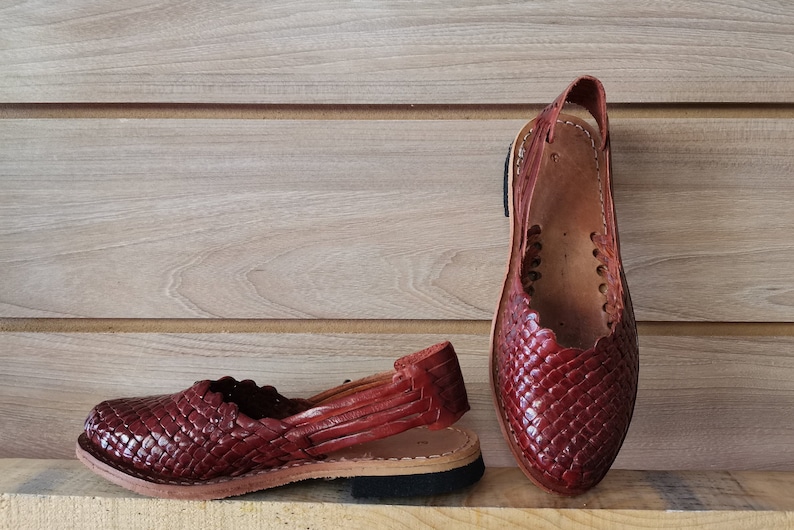 Puede incluir: Un par de sandalias de cuero marr&oacute;n con un dise&ntilde;o tejido. Las sandalias tienen una correa que va alrededor del tobillo y un dedo del pie cerrado.