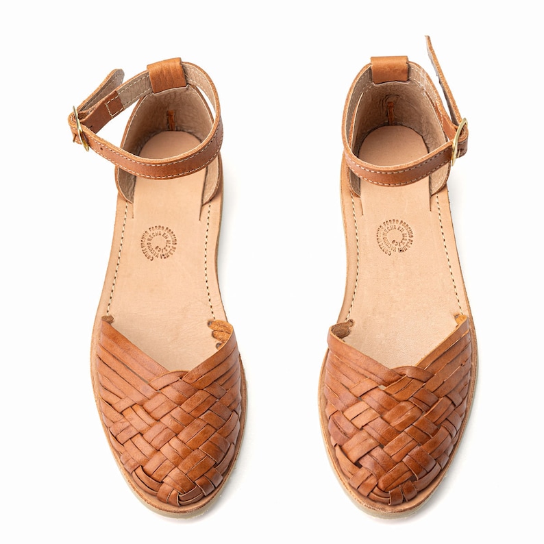 May include: A pair of brown leather sandals with woven straps. The sandals have an ankle strap with a buckle closure.