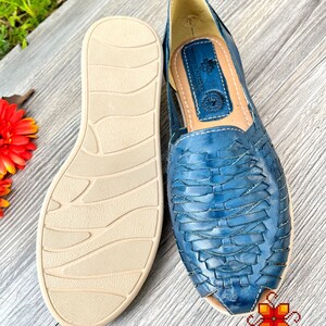 May include: A pair of blue leather sandals with a woven design. The sandals have a beige sole with a textured pattern.