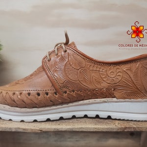 K&ouml;nnte beinhalten: Braune Lederschuhe mit aufwendigen Blumenstickereien und einer wei&szlig;en Plateau-Sohle. Die Schuhe haben einen Schn&uuml;rverschluss und sind in Mexiko hergestellt.