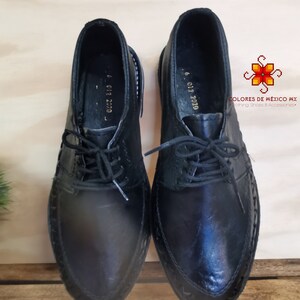 May include: A pair of black leather shoes with laces. The shoes have a pointed toe and a decorative stitch around the edge. The shoes are on a wooden surface.