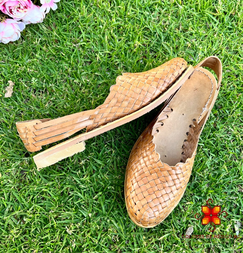 Puede incluir: Un par de sandalias de cuero trenzado de color marr&oacute;n claro. Las sandalias tienen un dise&ntilde;o sencillo con una tira trenzada sobre la parte superior del pie y una tira alrededor del tobillo.