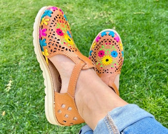 May include: A pair of brown leather sandals with colorful floral embroidery. The sandals have a cut-out design and a white platform sole.