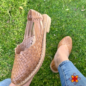 Puede incluir: Sandalias de cuero color marr&oacute;n claro con dise&ntilde;o tejido. Las sandalias tienen la punta cerrada y el tal&oacute;n abierto. Las sandalias las lleva puestas una persona con pantalones vaqueros azules.