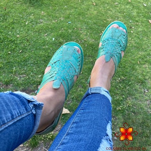 Puede incluir: Un par de sandalias de cuero azul turquesa con tiras tejidas. Las sandalias las lleva puesta una persona que lleva pantalones vaqueros azules.