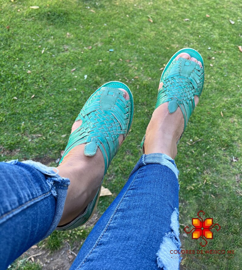 Puede incluir: Un par de sandalias de cuero azul turquesa con tiras tejidas. Las sandalias las lleva puesta una persona que lleva pantalones vaqueros azules.