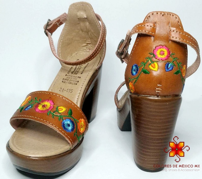 May include: Brown leather sandals with a platform heel and embroidered flowers in shades of pink, yellow, blue, and green. The sandals have an ankle strap with a buckle closure. The text "24-195" is visible on the sole.