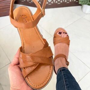 Pu&ograve; includere: Sandali in pelle color cuoio con cinturini incrociati e fibbia alla caviglia. I sandali hanno una suola platform e sono del marchio "Cuccia".
