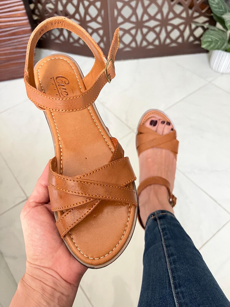 Pu&ograve; includere: Sandali in pelle color cuoio con cinturini incrociati e fibbia alla caviglia. I sandali hanno una suola platform e sono del marchio "Cuccia".