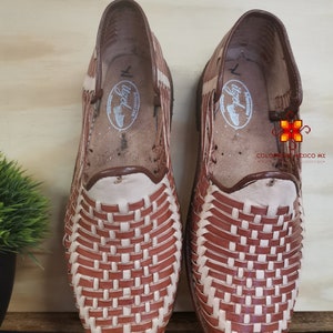 K&ouml;nnte beinhalten: Ein Paar braune Ledersandalen mit gewebtem Design. Die Sandalen haben ein wei&szlig;es Lederfutter und eine braune Ledersohle.
