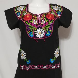 May include: Black embroidered blouse with colorful floral designs. The neckline features a pink tie closure. The embroidery includes white, pink, red, blue, and green thread.
