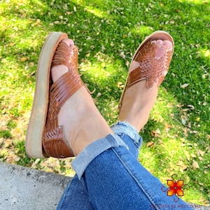 May include: Brown leather sandals with a woven design and a platform sole. The sandals are worn by a person wearing blue jeans.