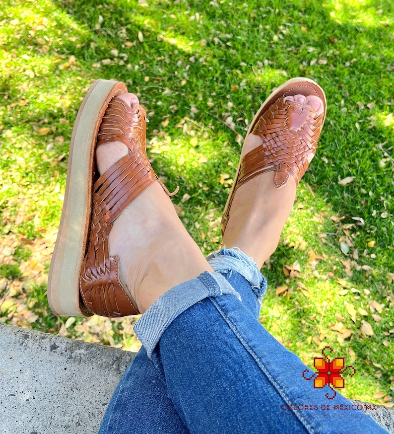 May include: Brown leather sandals with a woven design and a platform sole. The sandals are worn by a person wearing blue jeans.