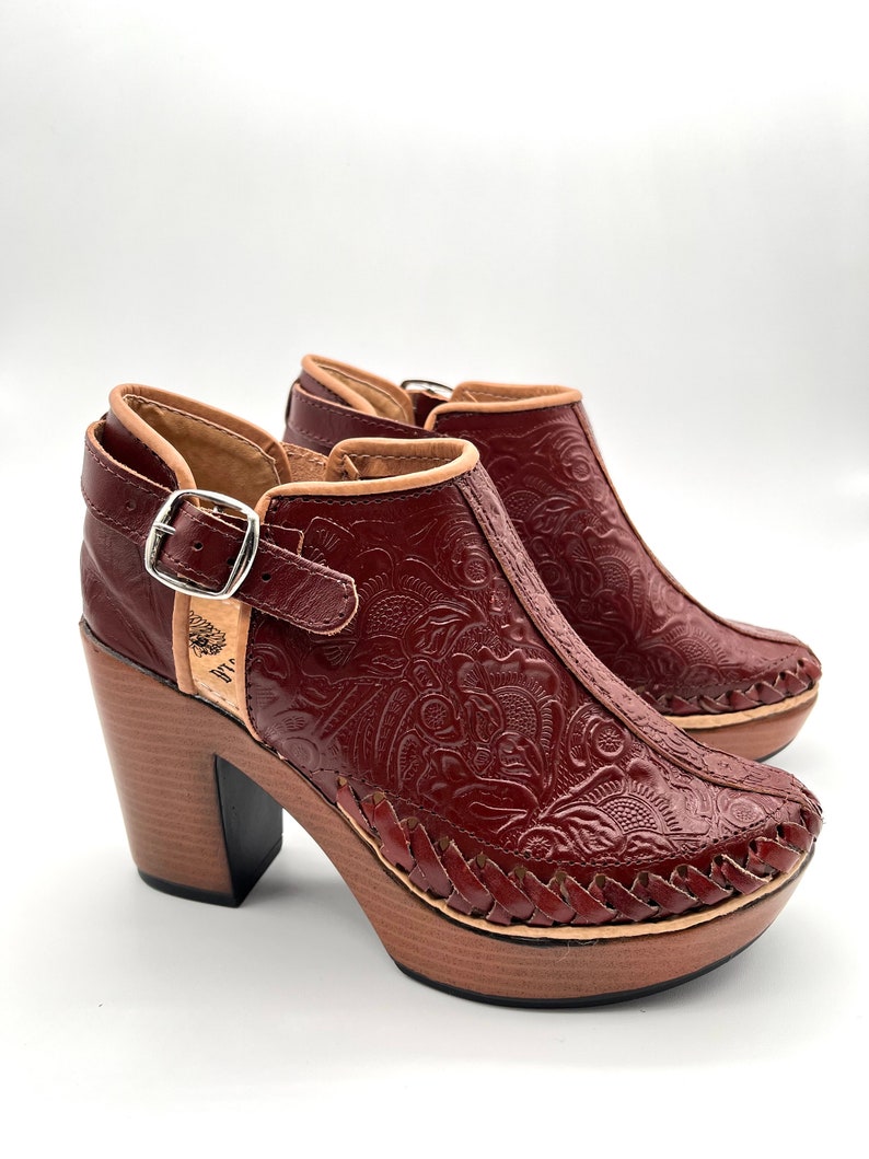 May include: A pair of brown leather ankle boots with a floral embossed design. The boots have a chunky wooden heel and a buckle closure.