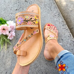 K&ouml;nnte beinhalten: Tanfarbene Ledersandalen mit Blumenstickerei in Rosa, Blau, Gr&uuml;n und Gelb. Die Sandalen haben eine Zehenschlaufe und einen Kn&ouml;chelriemen.
