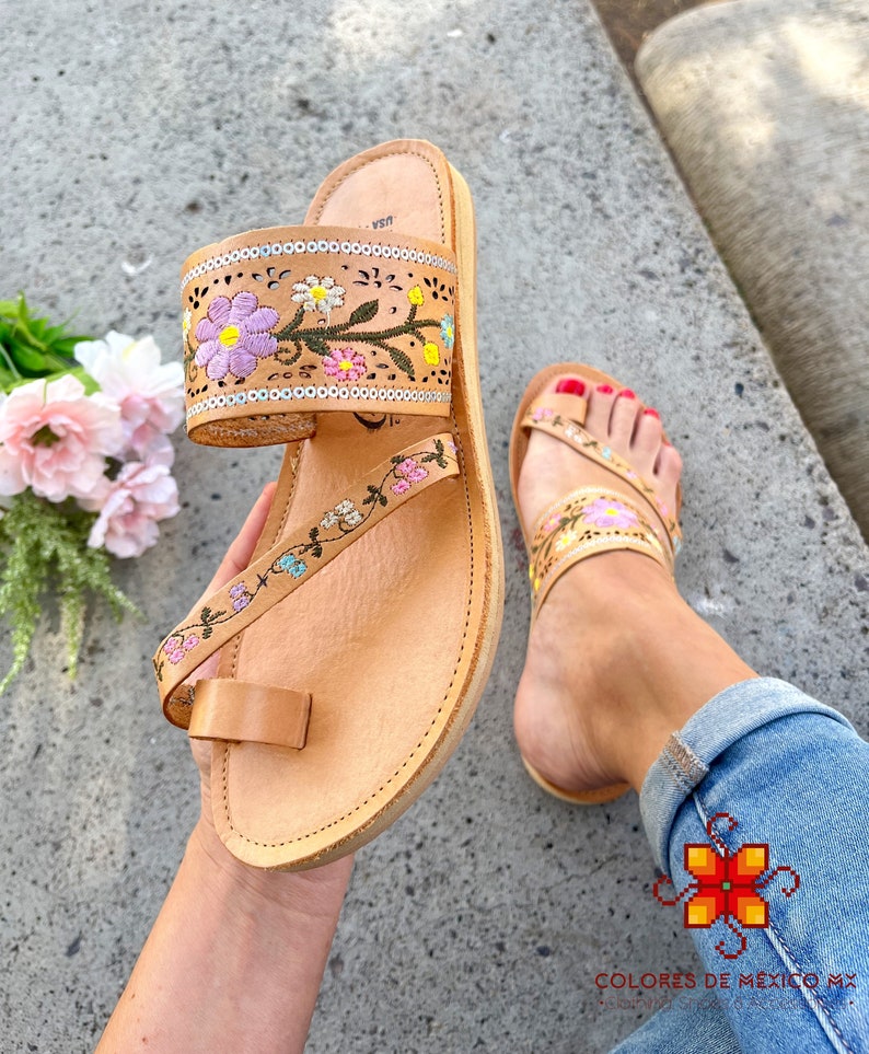 K&ouml;nnte beinhalten: Tanfarbene Ledersandalen mit Blumenstickerei in Rosa, Blau, Gr&uuml;n und Gelb. Die Sandalen haben eine Zehenschlaufe und einen Kn&ouml;chelriemen.