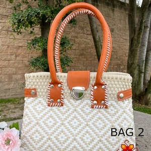 May include: A white and tan woven tote bag with a brown leather handle and a silver clasp. The bag has a diamond pattern and the text "BAG 2" is visible in the lower right corner.