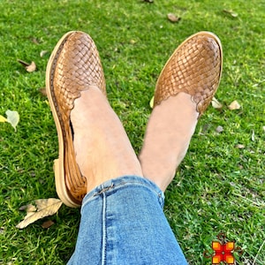 Puede incluir: Un par de sandalias de cuero marr&oacute;n con un dise&ntilde;o tejido. Las sandalias son usadas por una persona sentada en una superficie cubierta de hierba.