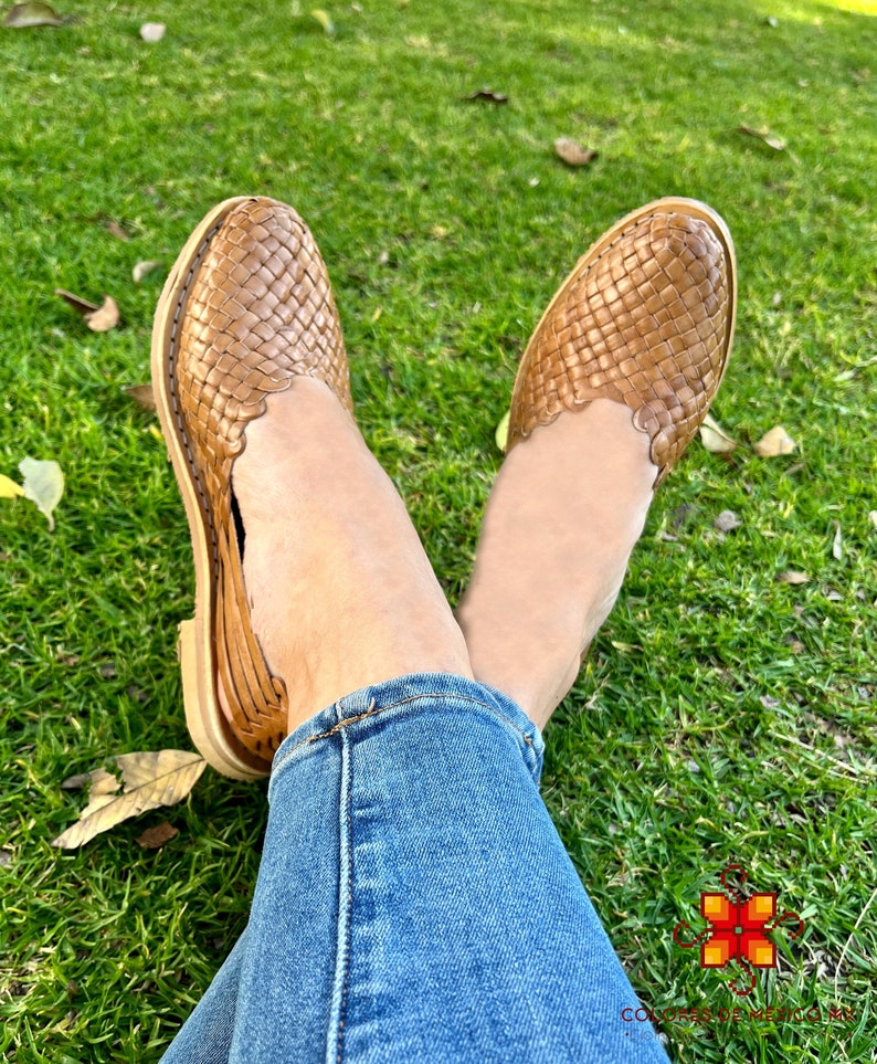 Puede incluir: Un par de sandalias de cuero marr&oacute;n con un dise&ntilde;o tejido. Las sandalias son usadas por una persona sentada en una superficie cubierta de hierba.