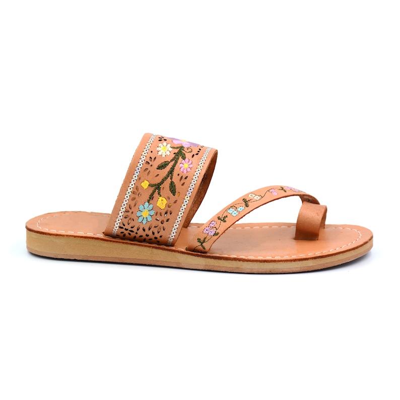 K&ouml;nnte beinhalten: Tannfarbene Ledersandalen mit floralem Stickmuster. Die Sandalen haben einen Zehensteg und einen Riemen, der um den Kn&ouml;chel geht.