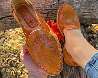 May include: A pair of brown leather sandals with a sunflower design. The sandals are made in Mexico and have a comfortable fit.