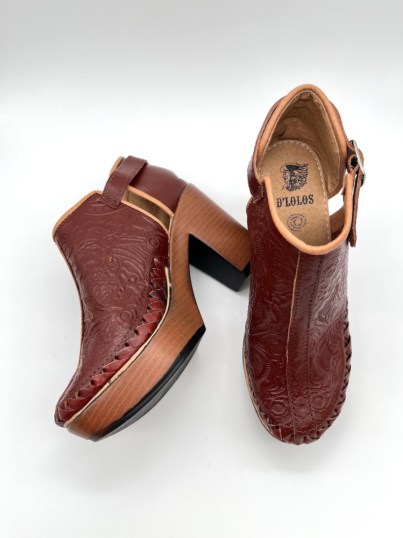 May include: A pair of brown leather ankle boots with a floral embossed design. The boots have a wooden platform and a chunky heel. The boots are made by D'Lolos.
