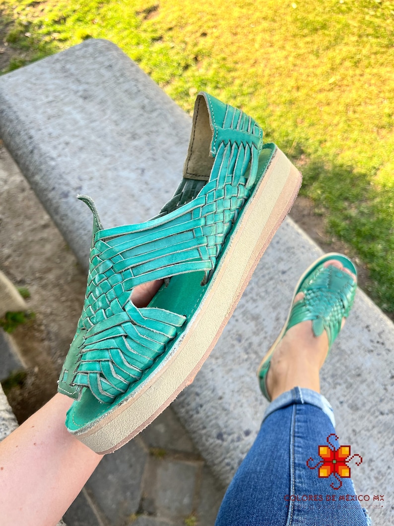 Puede incluir: Sandalias de cuero color turquesa con dise&ntilde;o tejido y suela de plataforma. Las sandalias est&aacute;n siendo sostenidas por una persona que lleva pantalones vaqueros azules.